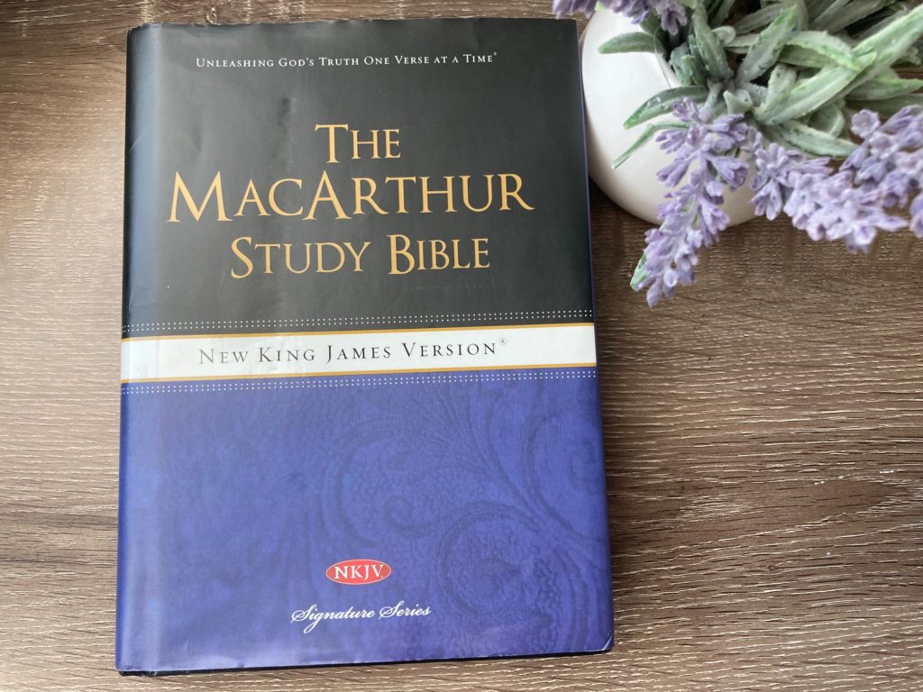 The MacArthur Study Bible on a table next to purple flowers.