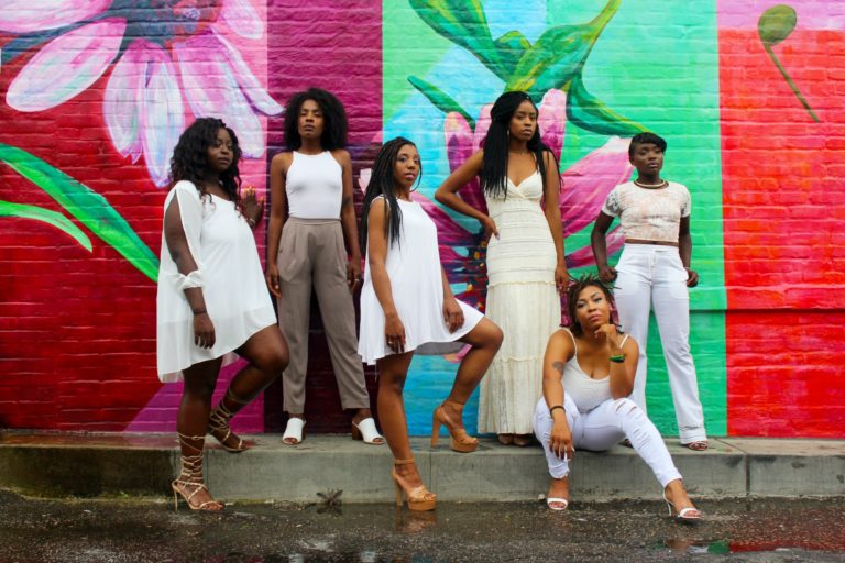 Group of black girlfriends posing against colorful mural, representing friendships.