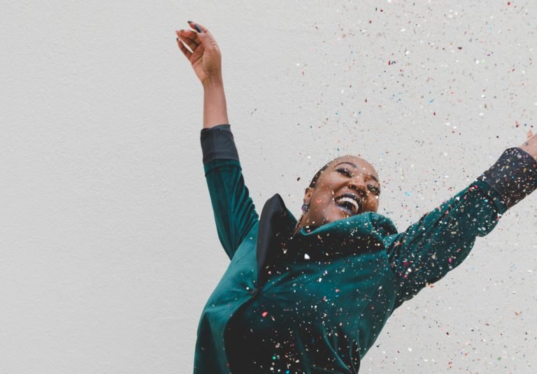 Black woman wearing green suit celebrating with arms lifted and confettio